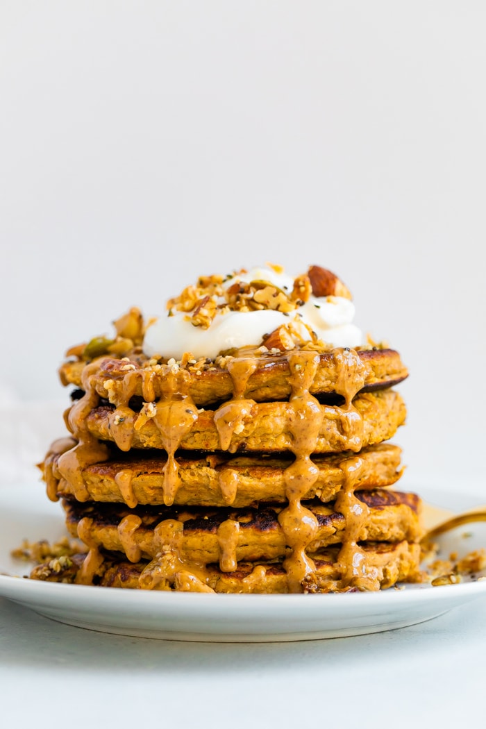 Stack of butternut squash pancakes topped with peanut butter, maple syrup, granola, and yogurt.