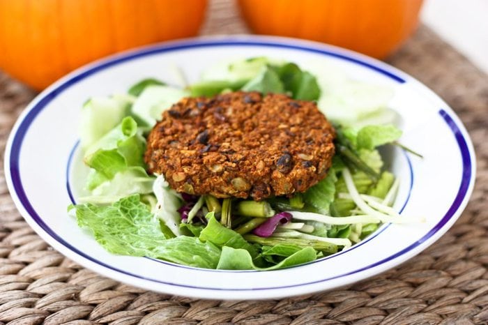 Curried Pumpkin Black Bean Burger on a plate of greens with pumpkins in the background on the table.