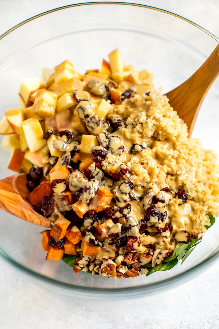 Ingredients for the fall harvest salad in a glass bowl being tossed with the apple cider vinegar tahini dressing.