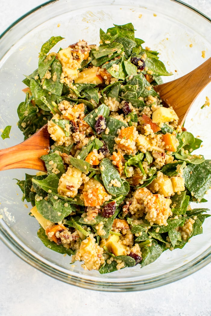 Tossed fall harvest spinach salad in a glass bowl with wooden spoons.