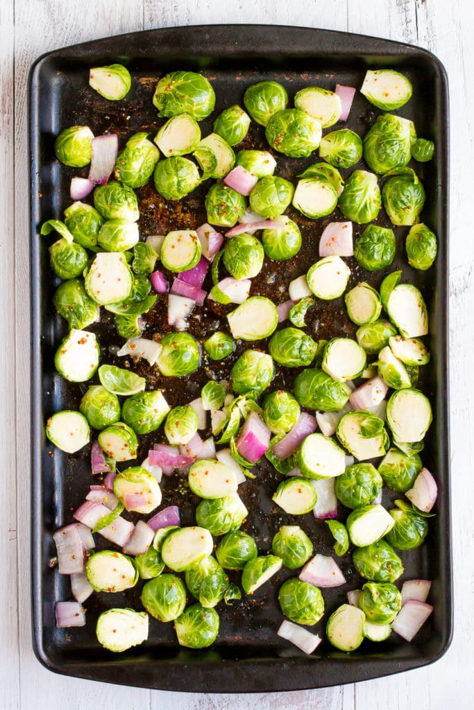 Brussels sprouts and red onion on a baking stone before roasting.