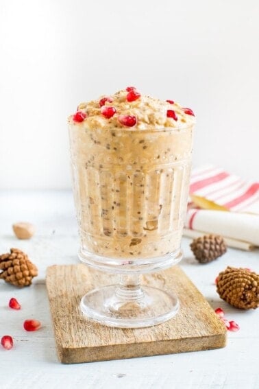 Glass of healthy eggnog overnight oats, topped with pomegranate seeds.