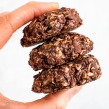 A hand holding a stack of three peanut butter chocolate no bake cookies.