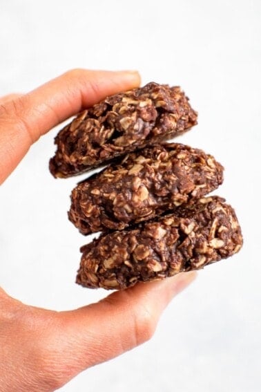 A hand holding a stack of three peanut butter chocolate no bake cookies.