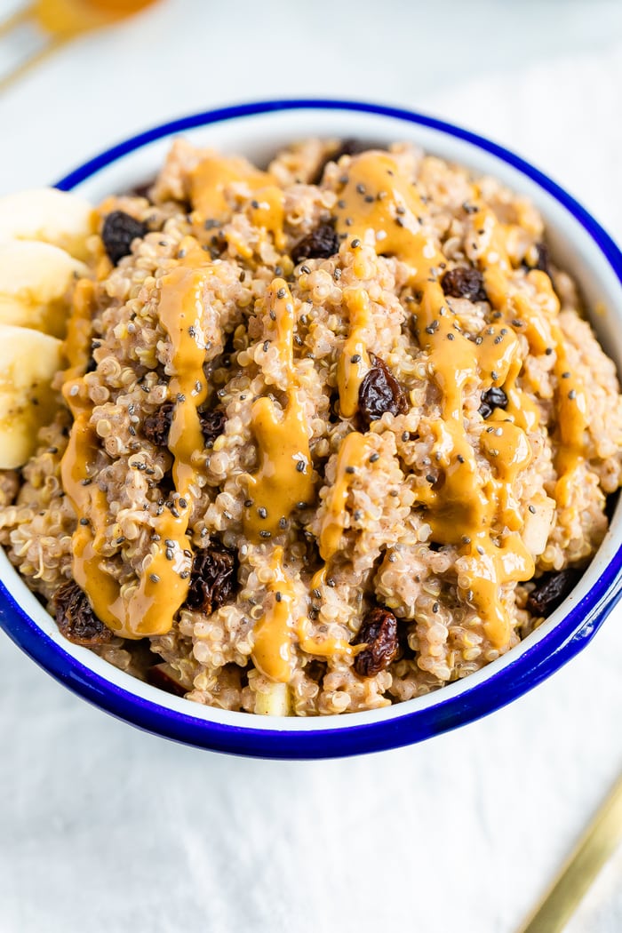 Bowl of cinnamon breakfast quinoa, topped with raisins, chia seeds, peanut butter, and banana slices.