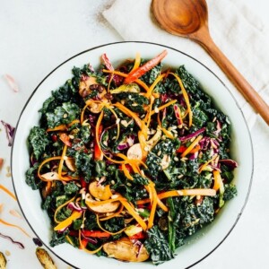 Overhead shot of single serving of detox kale salad with sliced avocado on top. Wooden spoon is on the side of the bowl.