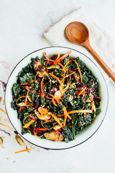 Overhead shot of single serving of detox kale salad with sliced avocado on top. Wooden spoon is on the side of the bowl.