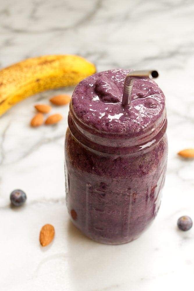 Blueberry almond smoothie in a mason jar with a metal straw. Almonds, berries and a banana are to the side.