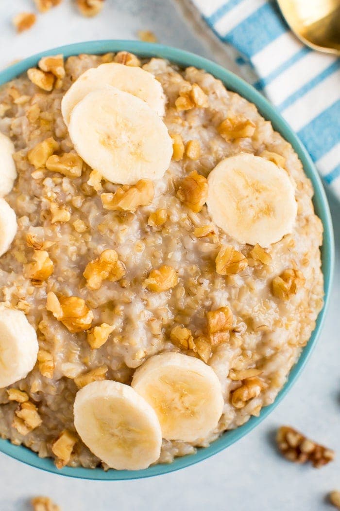 Up close shot of creamy steel cut oats topped with banana slices and walnuts in a blue bowl. 