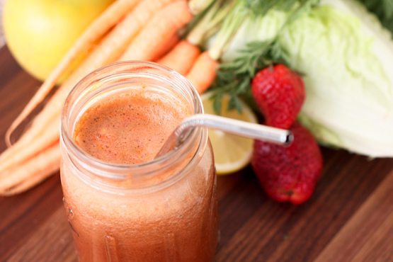 Strawberry Sunrise Juice served in a mason jar next fresh juice ingredients on wood cutting board.