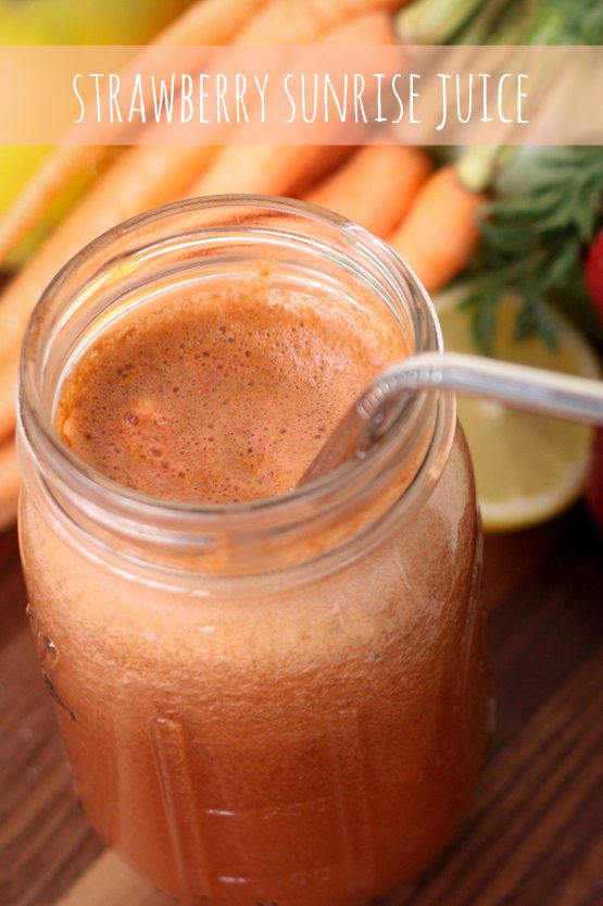 Strawberry Sunrise Juice served in a mason jar with stainless steel spoon, bunch of carrots in background.