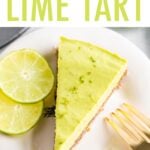 Slice of avocado lime tart on a plate with a gold fork and two slices of lime.