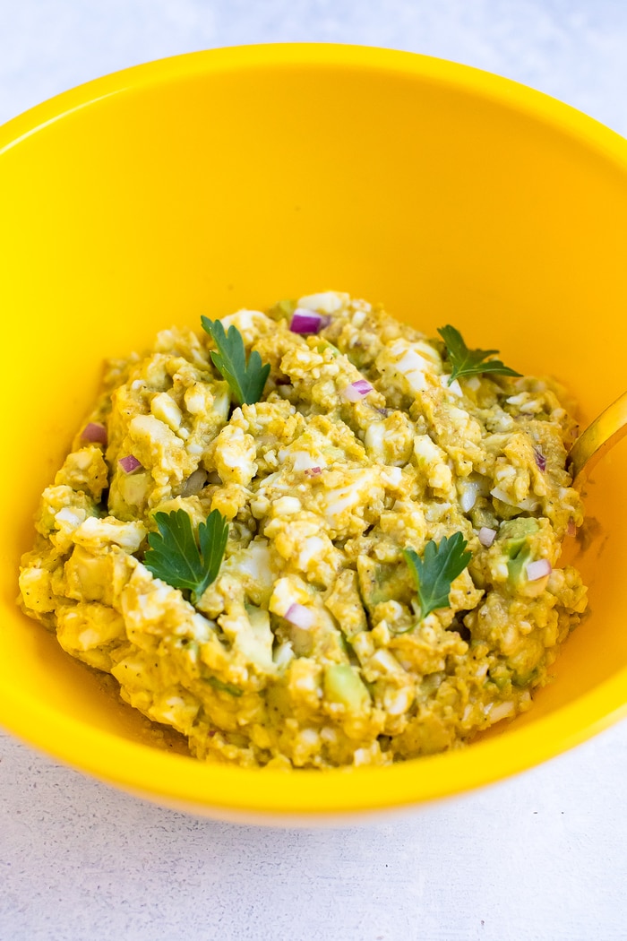 Curried avocado egg salad in a yellow bowl with parsley leaves on top. 