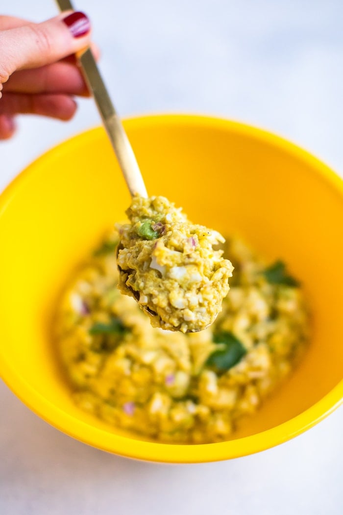 Curried avocado egg salad on a gold spoon in a yellow bowl. 