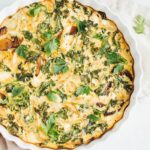 Crustless quiche with kale, onions, mushrooms and feta in a white baking dish on a rustic napkin.