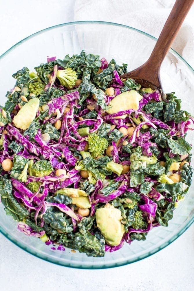 Salad with kale, cabbage, avocado, broccoli, chickpeas, and a nutritional yeast goddess dressing in a bowl.