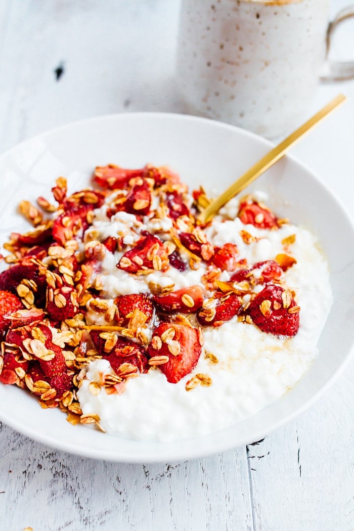 A closeup of a bowl of roasted strawberries on top of cottage cheese.