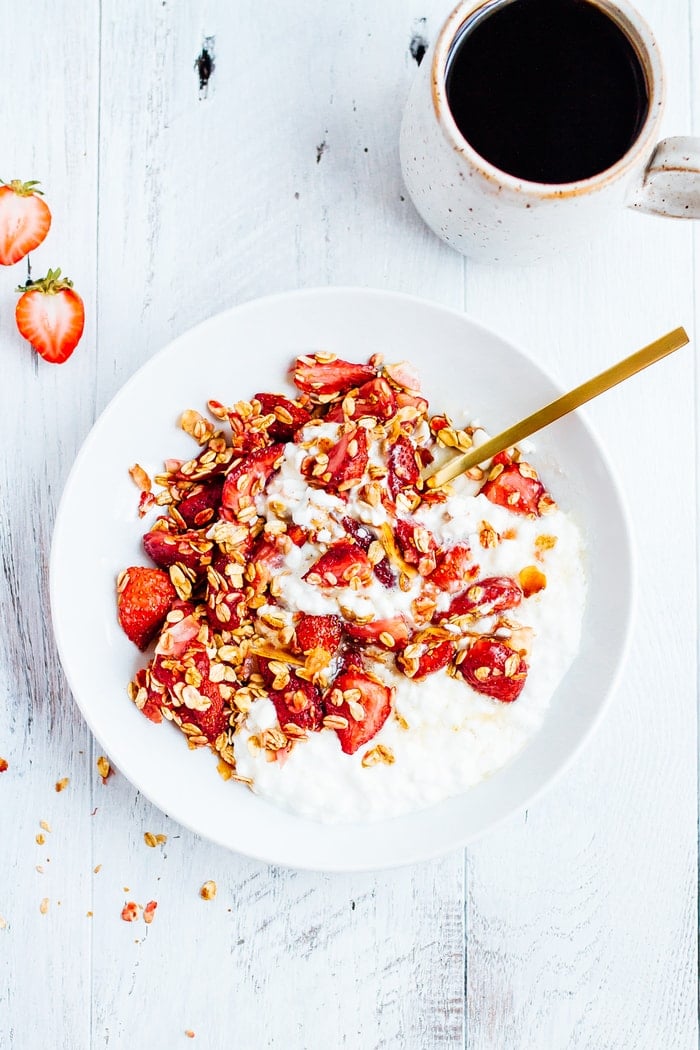 An overhead bowl of a plate of roasted strawberry cottage cheese. A cup of coffee is next to the bowl.