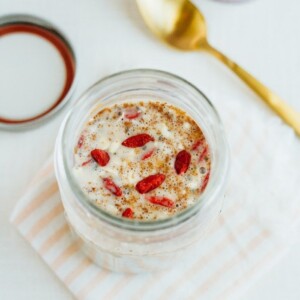 A jar filled with almond milk and superfood cereal sitting on a folded peach and white striped napkin. Jar lid and gold spoon in the background.