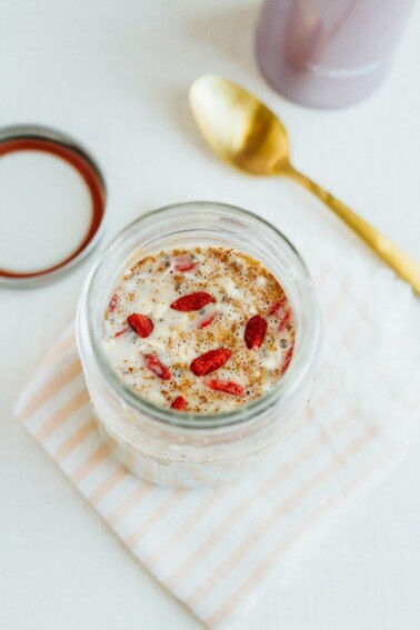 A jar filled with almond milk and superfood cereal sitting on a folded peach and white striped napkin. Jar lid and gold spoon in the background.