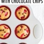 Strawberry chocolate chip protein muffins in red cupcake liners in a muffin tin. Muffins are topped with chopped strawberries and mini chocolate chips.