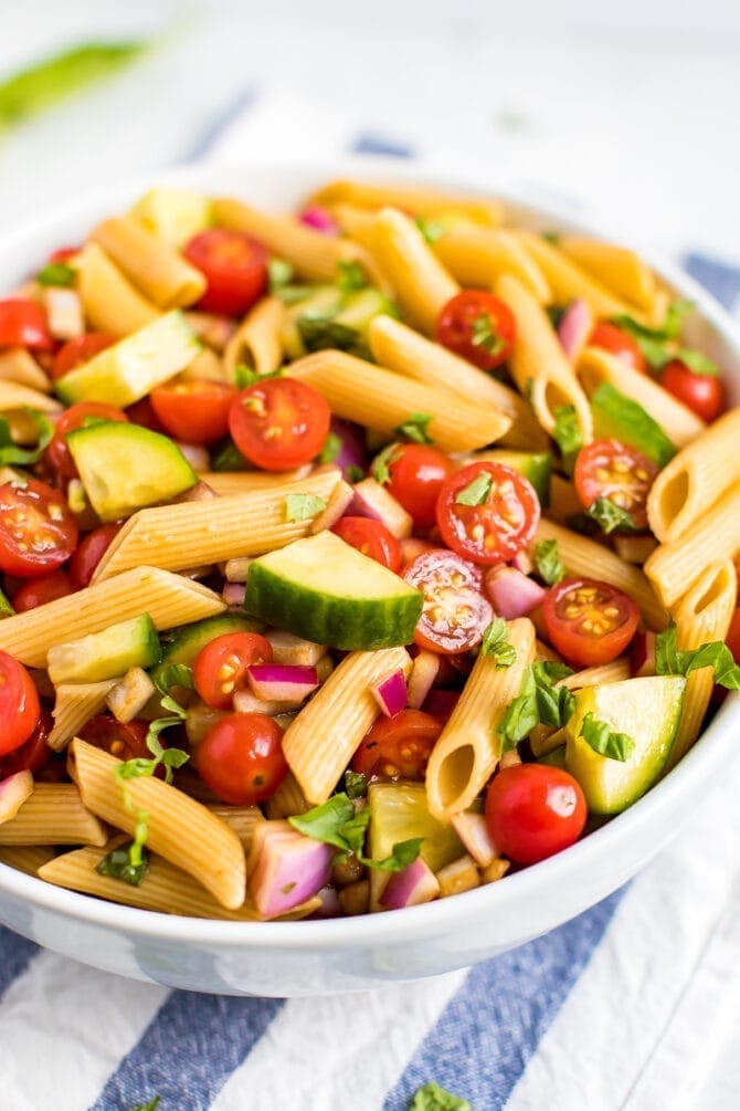 Bowl of penne pasta salad with basil, cucumbers, tomatoes and red onions.