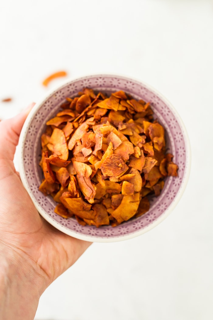 Hand holding a pink bowl filled with Vegan Coconut Bacon.