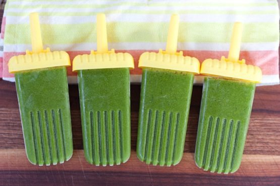 Green Smoothie Protein Popsicles on wood cutting board with colorful dish towel.