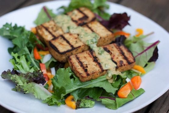 A plate with basil lemon tofu on a bed of mixed greens.