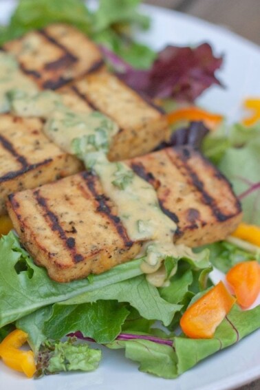 A plate with basil lemon tofu on a bed of mixed greens.