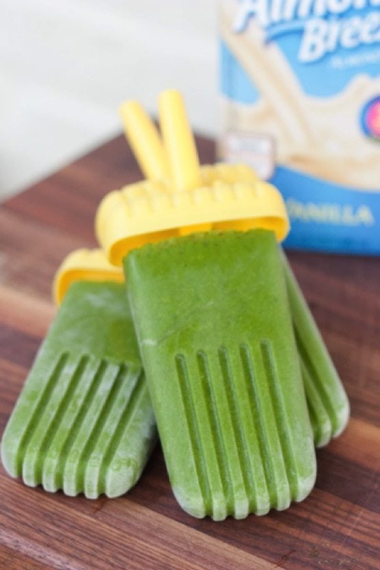 Green Smoothie Protein Popsicles on wood cutting board, almond milk container in background.