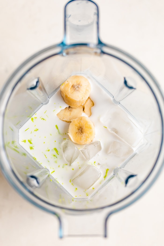 Vitamix blender overhead shot with coconut milk, banana chunks, ice and lime zest.