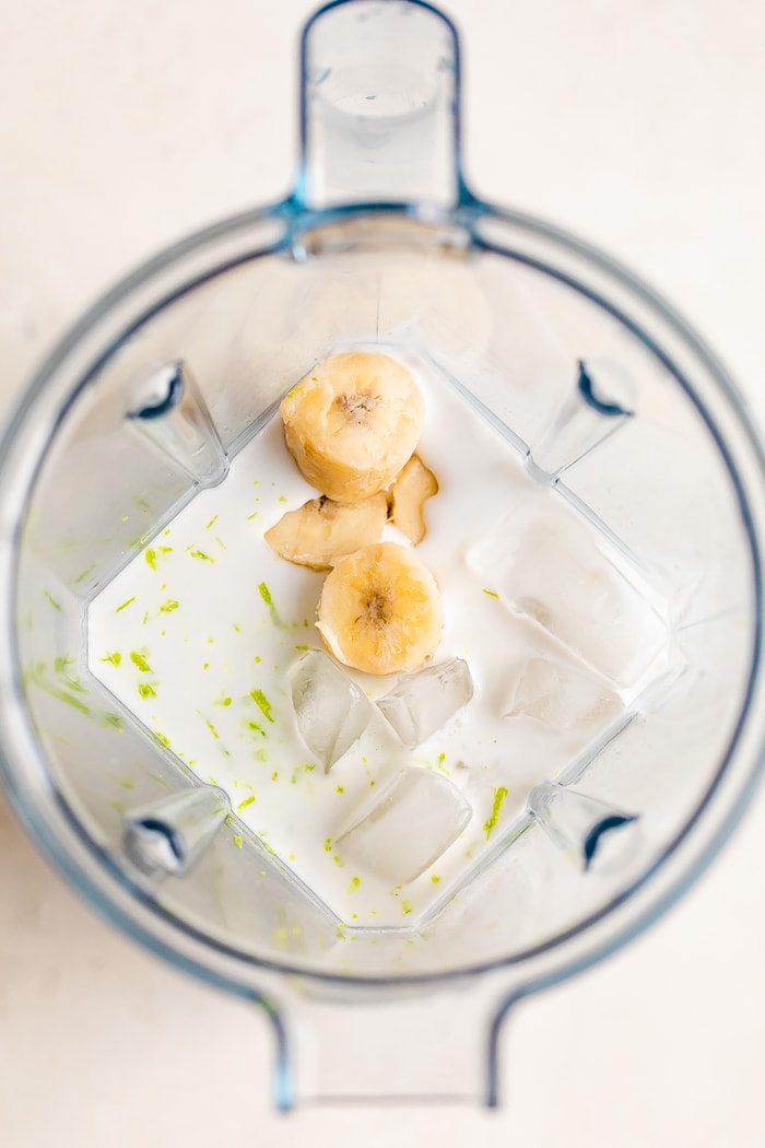 Vitamix blender overhead shot with coconut milk, banana chunks, ice and lime zest.