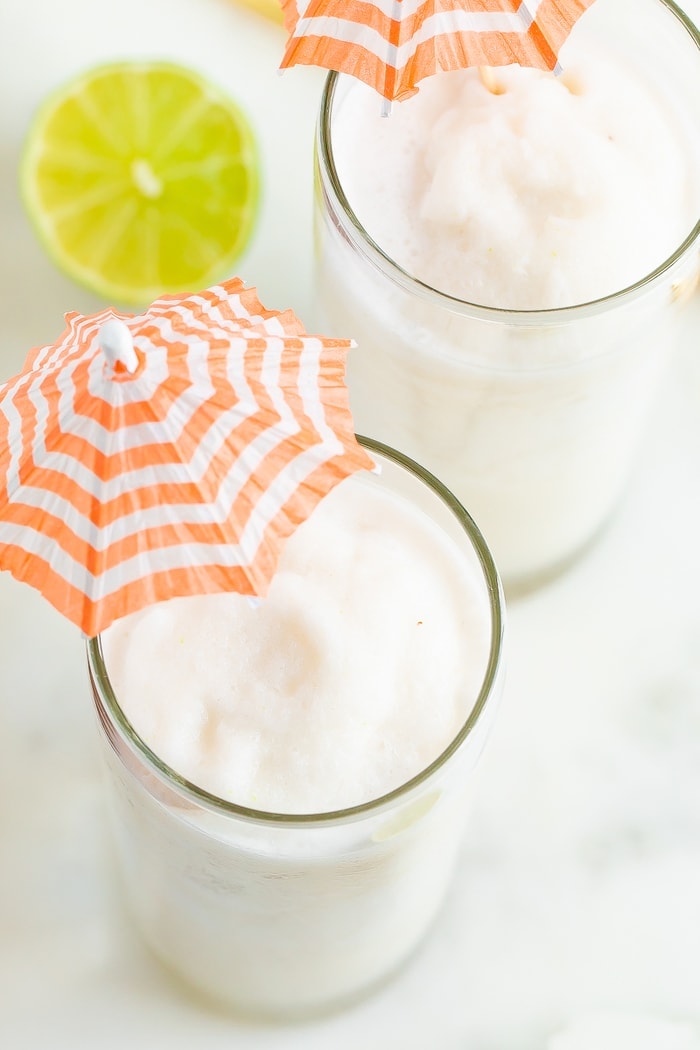 Close up overhead shot with two skinny coconut daiquiri cocktails in tall glasses with orange and white striped cocktail umbrellas.