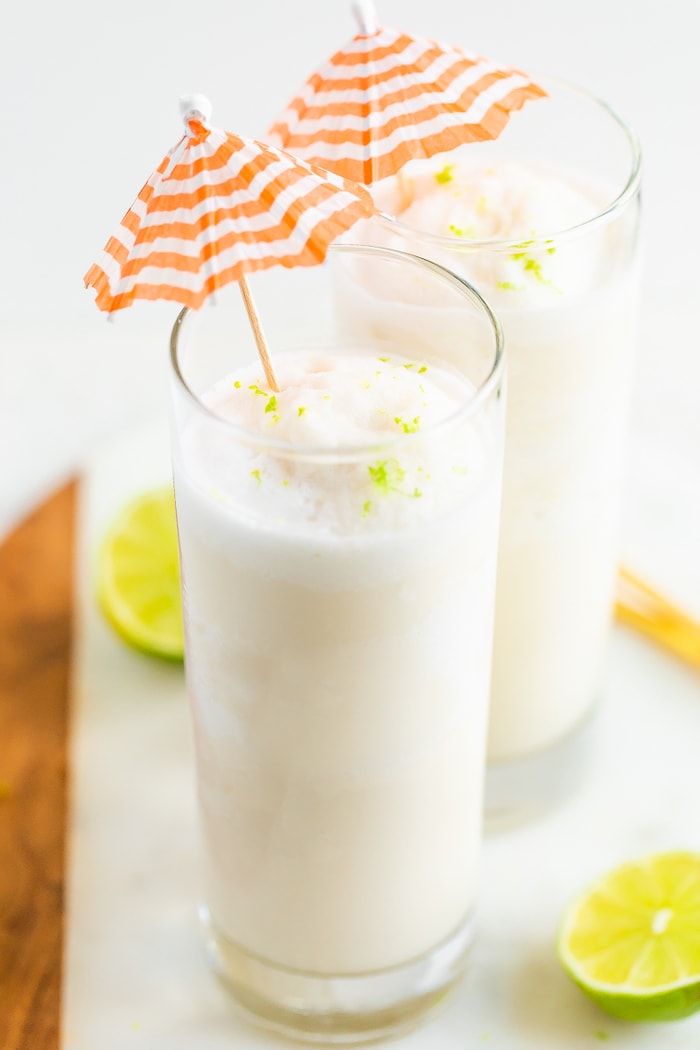 Two skinny coconut daiquiri cocktails in tall glasses with orange and white striped cocktail umbrellas.