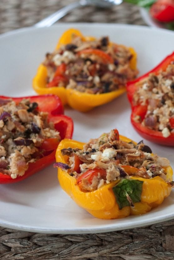 Four red and yellow tuna stuffed peppers on a white plate.