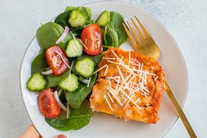 Slice of zucchini tofu lasagna topped with parmesan cheese. Served on a plate with a green salad.