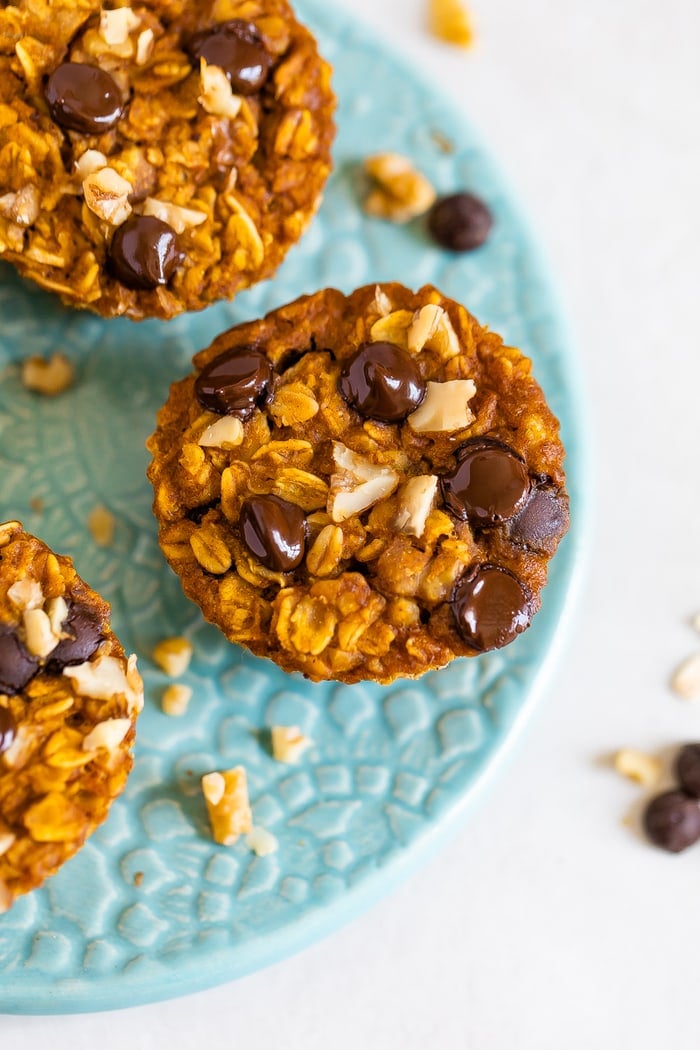 Three baked pumpkin oatmeal cups on a plate. Oatmeal cups are topped with walnuts and chocolate chips.