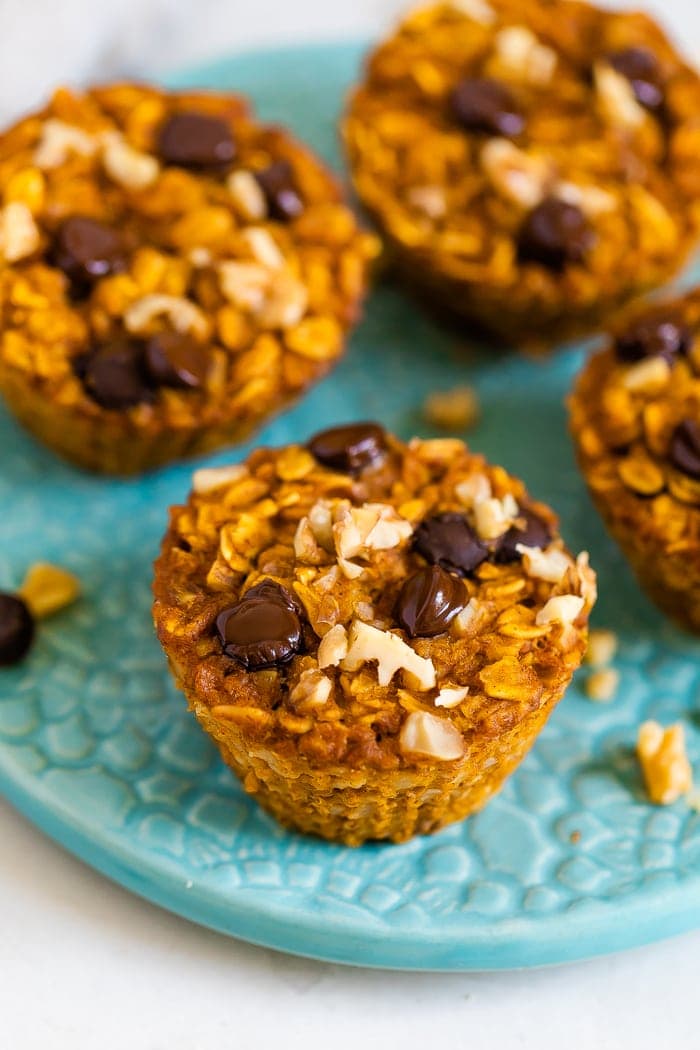 Four baked pumpkin oatmeal cups on a plate. Oatmeal cups are topped with walnuts and chocolate chips.