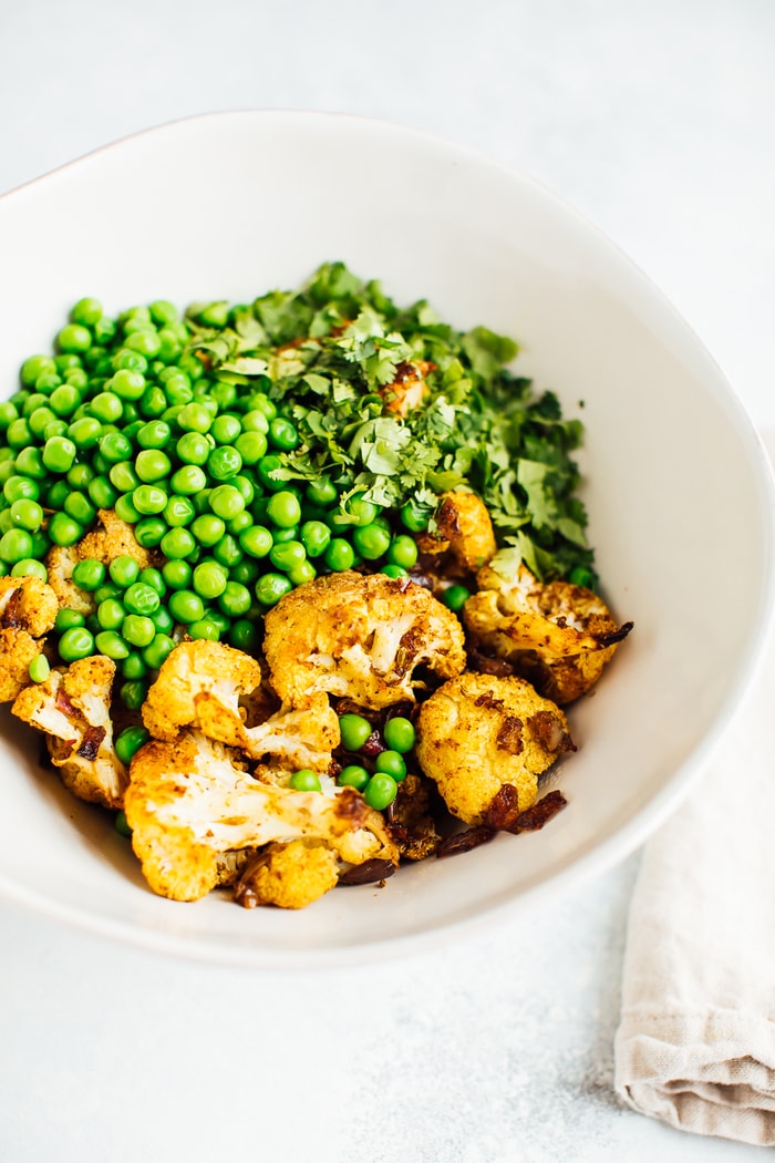 Curry roasted cauliflower, green peas and cilantro in a large white bowl. 