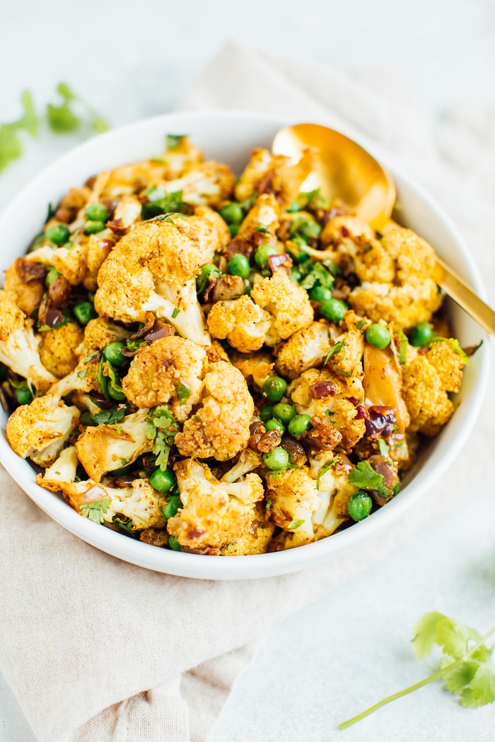 A curried cauliflower salad with green peas and cilantro in a large white bowl with a gold spoon. 