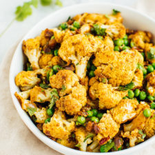 A curried cauliflower salad with green peas and cilantro in a large white bowl.