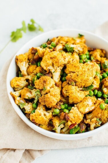 A curried cauliflower salad with green peas and cilantro in a large white bowl.