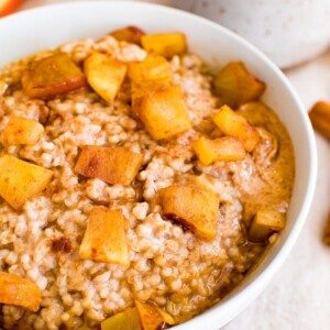 Bowl of healthy apple cinnamon oatmeal made with steel cut oats and topped with cinnamon and chunks of apple, and a dollop of peanut butter.