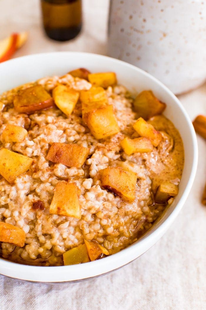 Bowl of healthy apple cinnamon oatmeal made with steel cut oats and topped with cinnamon and chunks of apple, and a dollop of peanut butter.