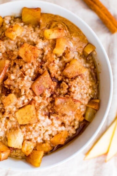 Healthy apple cinnamon oatmeal in bowl topped with apple chunks and cinnamon.