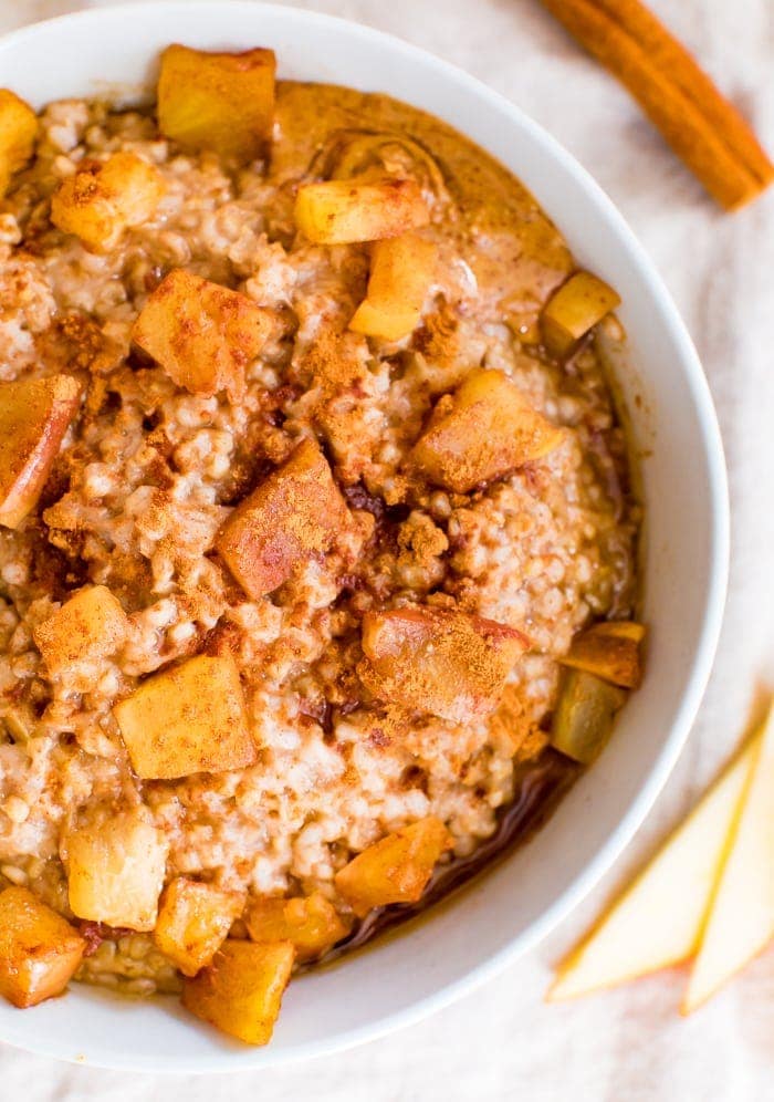 Healthy apple cinnamon oatmeal in bowl topped with apple chunks and cinnamon.