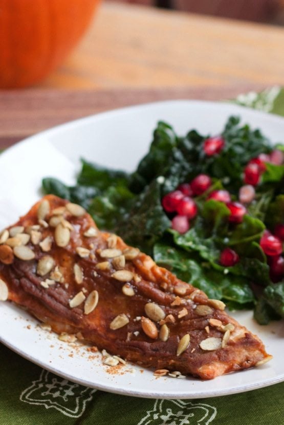 Pumpkin Spice salmon topped with seeds, and next to a kale and pomegranate salad on a plate.