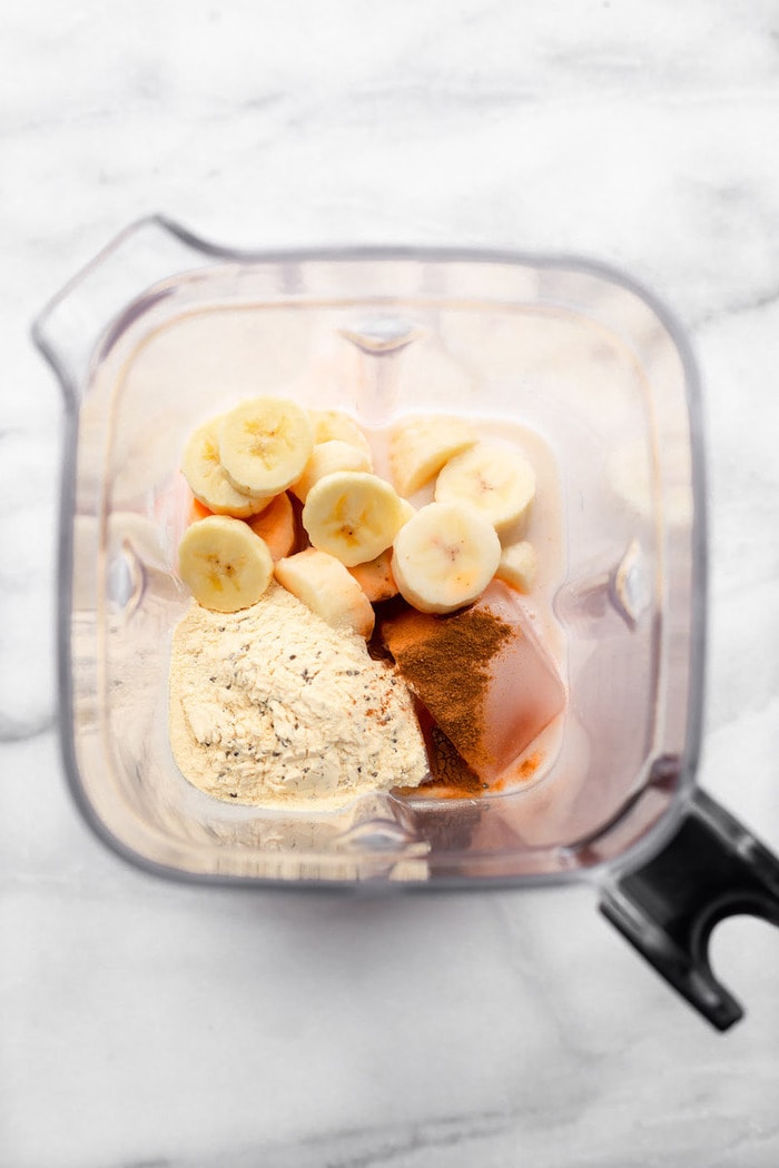 Ingredients for a carrot cake protein smoothie in a blender before blending-- banana, carrot juice, protein powder and cinnamon