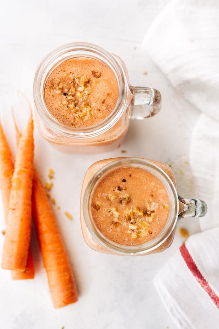 Bird's eye photo of two mason jar mugs filled with carrot cake smoothie and topped with chopped walnuts.
